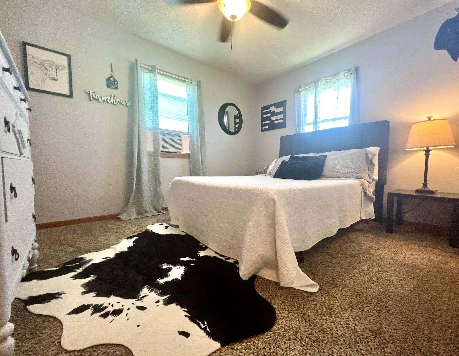 Bedroom one with a queen bed, cowhide rug, antique dresser and two bright windows