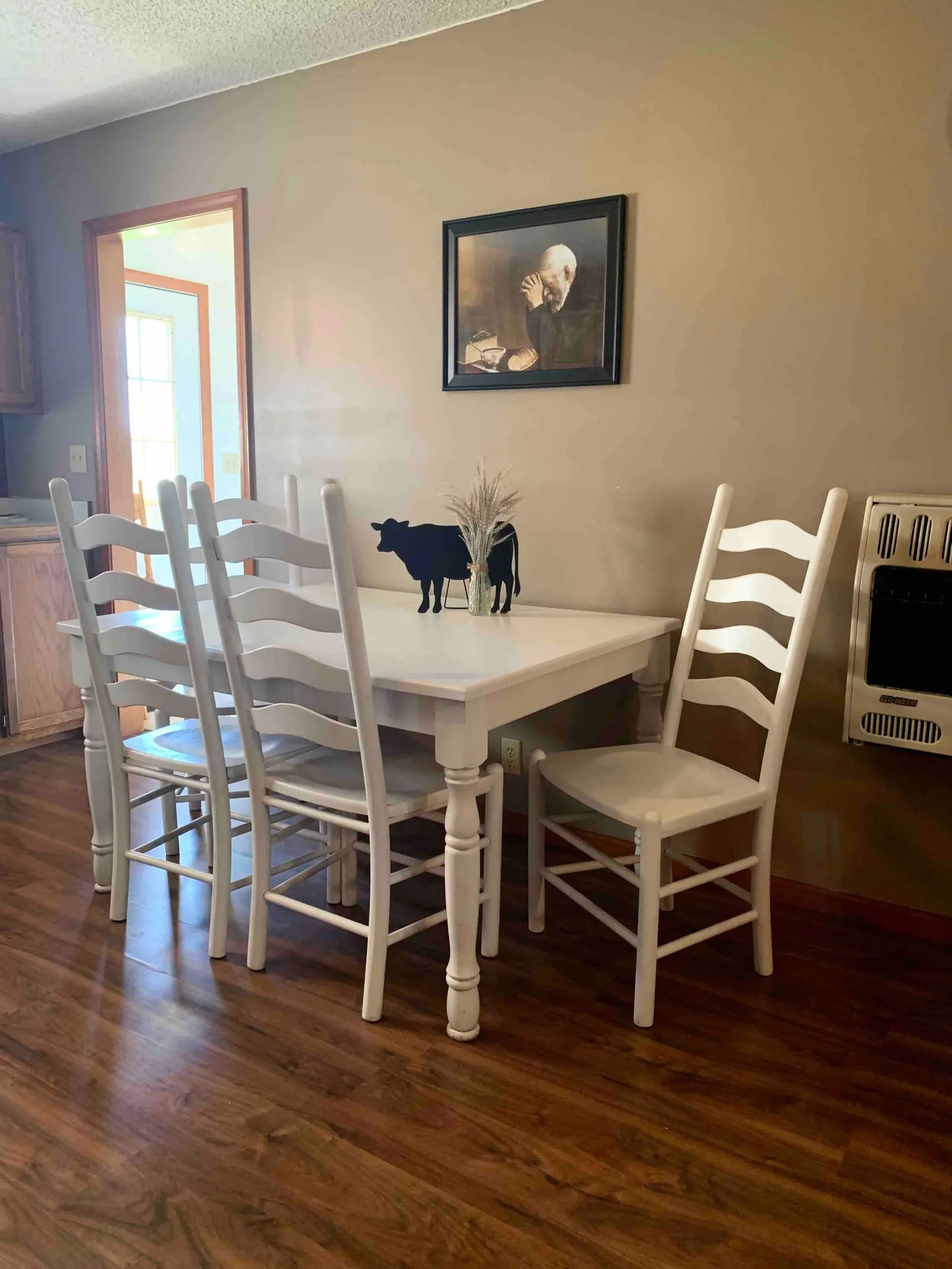 Dining room with a white farmhouse table and four ladder-back chairs on hardwood floors