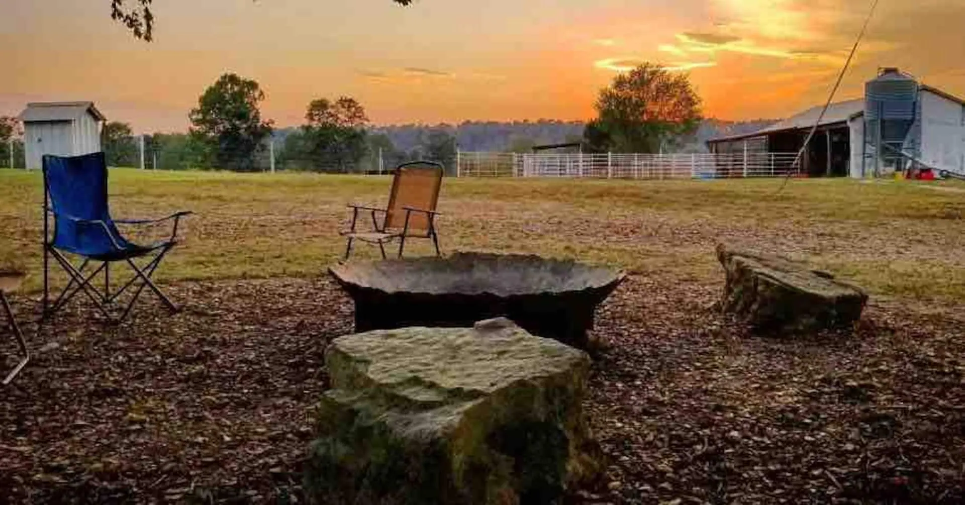 Cast-iron tumbling crusher from a local rock quarry repurposed as a fire pit, ringed with camp chairs and stone seats at sunset