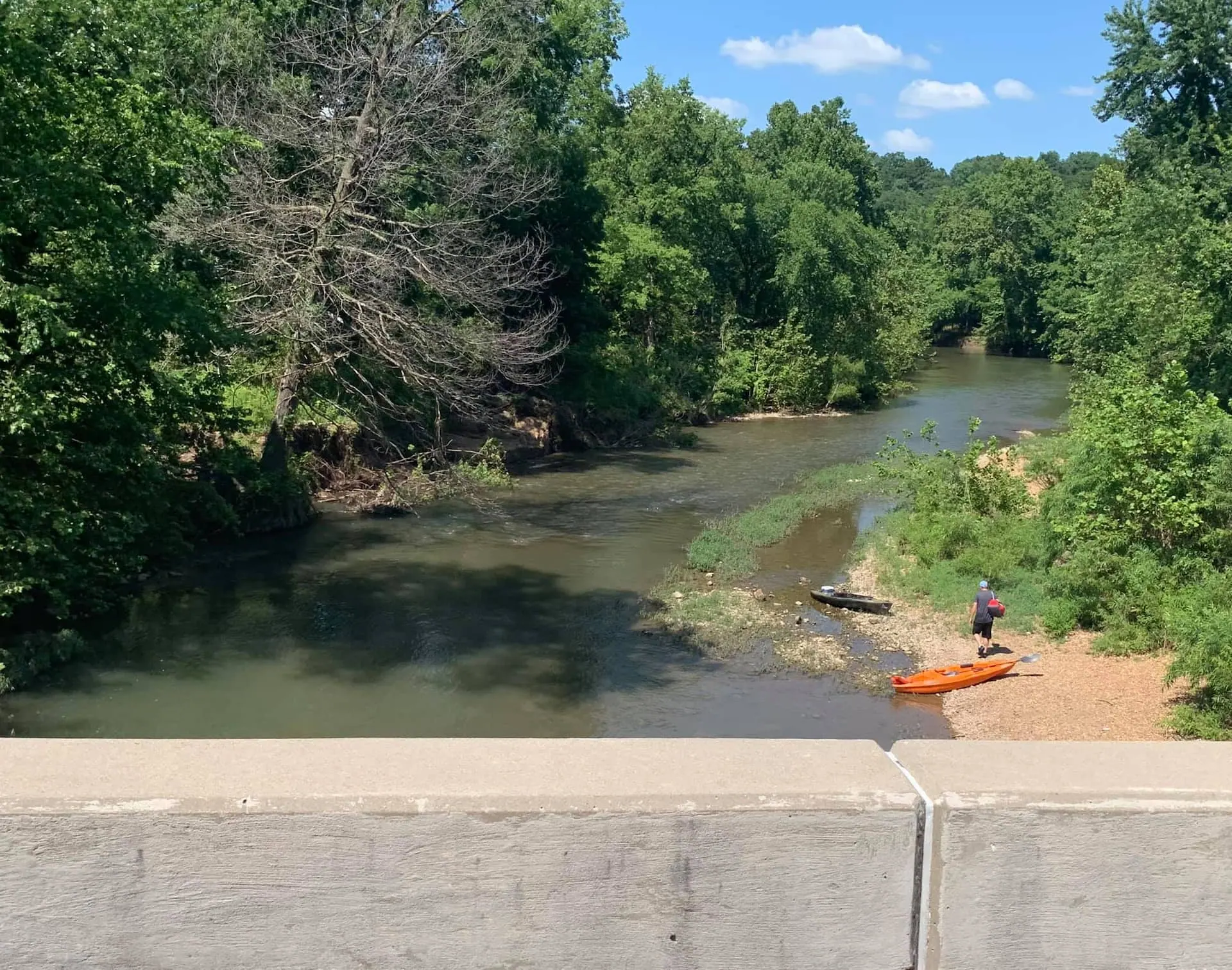 Looking down at the Sac River from the bridge with a kayak pulled up on the bank, the start of the float back to the gravel bar behind the house