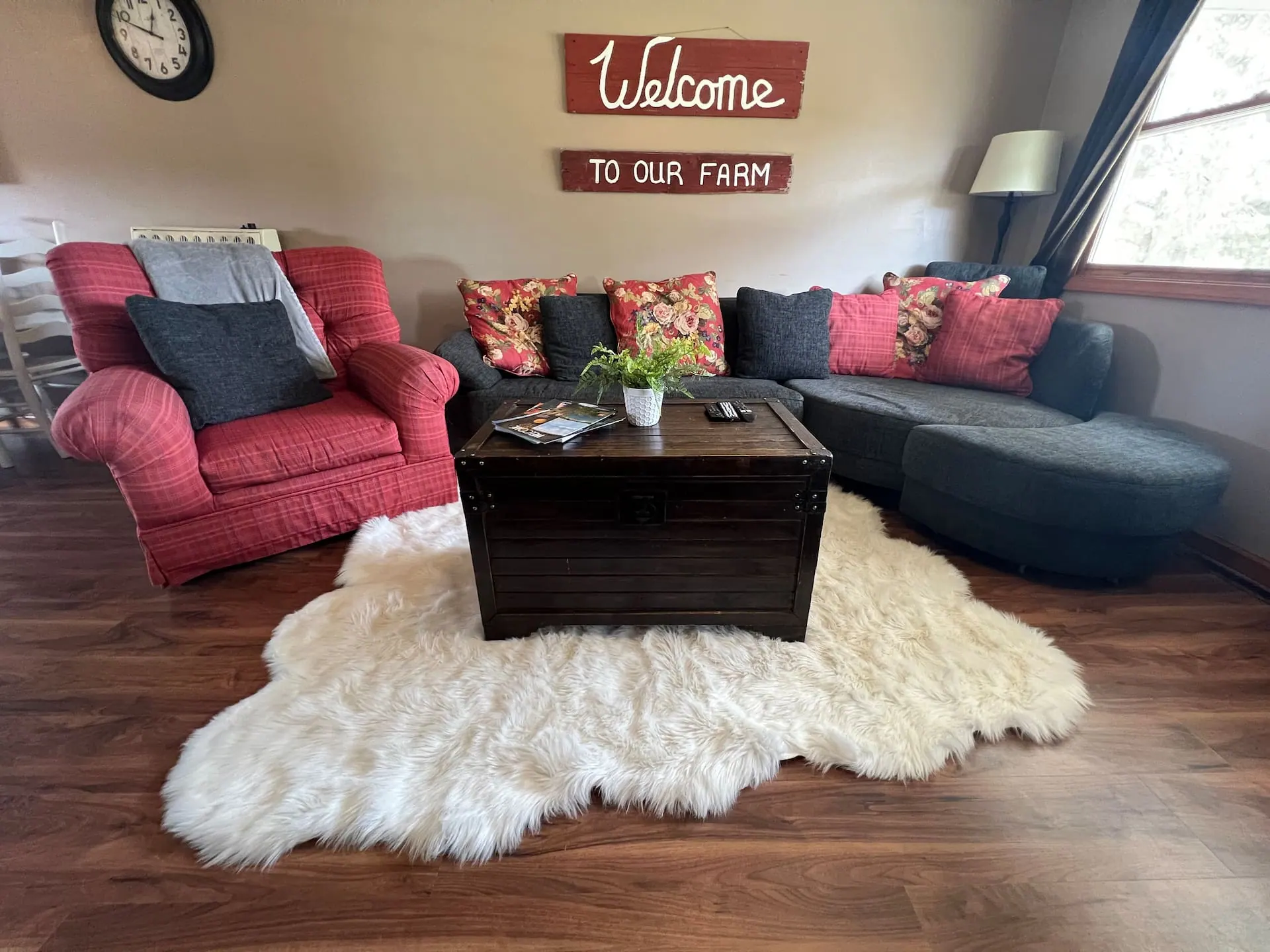Farmhouse living room with a gray sectional, red armchair, sheepskin rug and a wooden "Welcome to our farm" sign