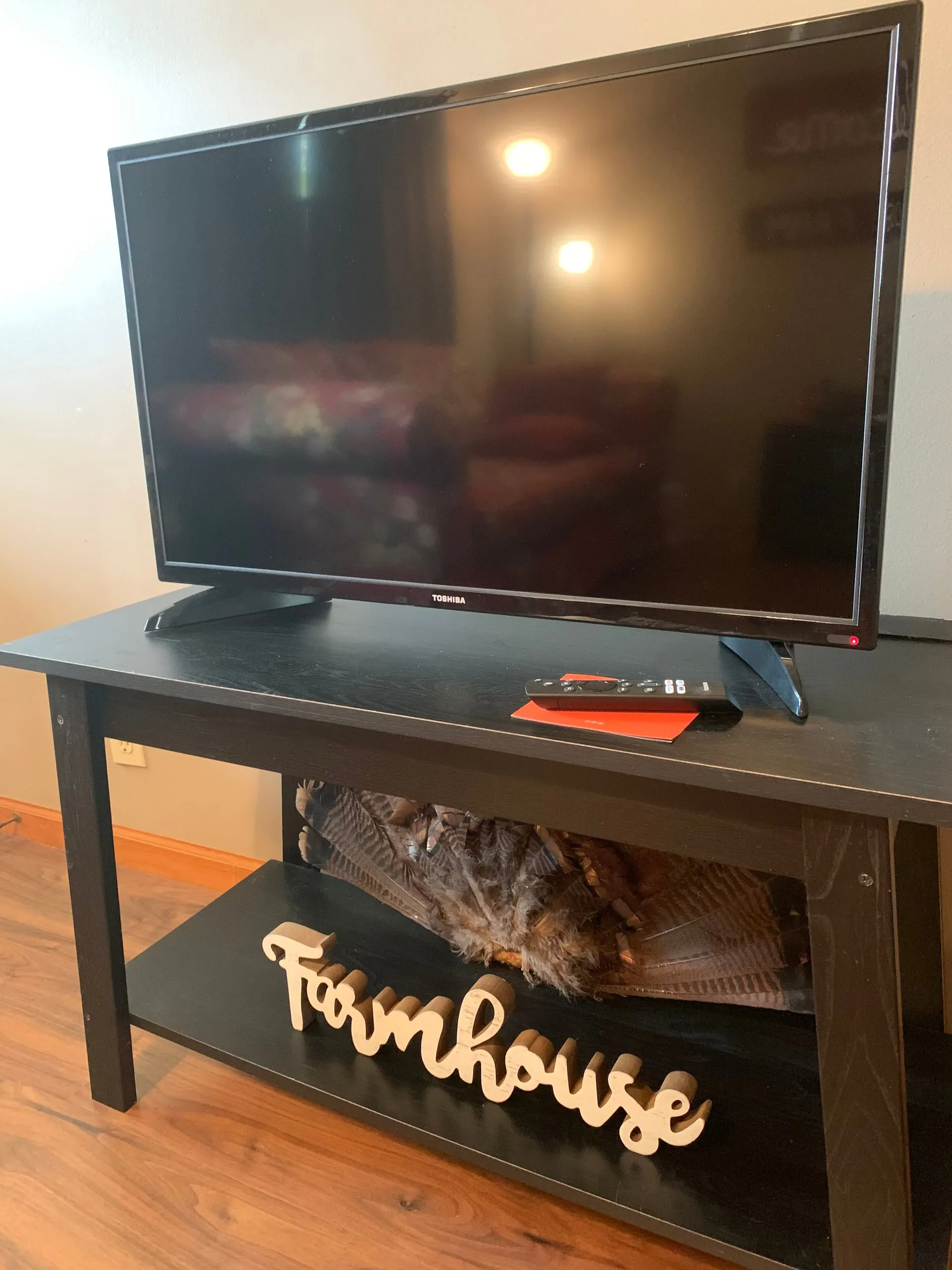 Flat-screen television on a console with a carved wooden "Farmhouse" sign in the living room